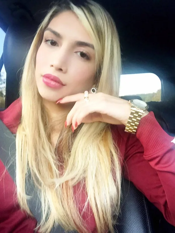 Portrait d'une femme aux cheveux blonds assise dans une voiture, portant un sweat-shirt rouge et regardant l'objectif.
