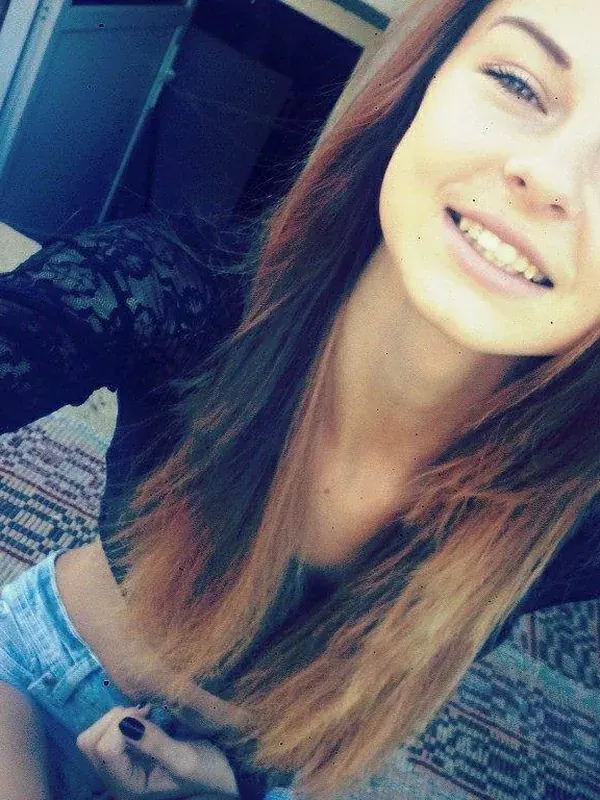Portrait d'une jeune femme souriante en chemise noire et short en jean, prenant un selfie à l'intérieur.