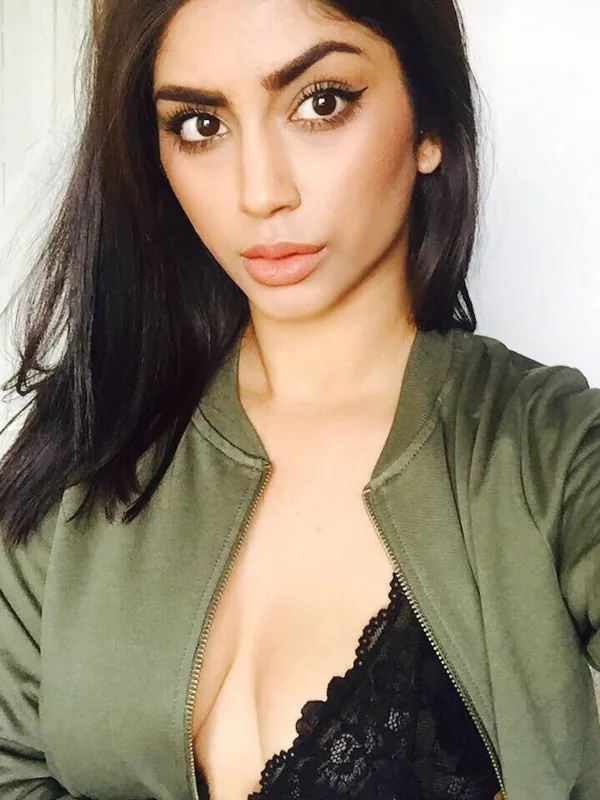Portrait en selfie d'une femme aux cheveux noirs portant une veste verte et un haut noir en dentelle, regardant l'objectif.