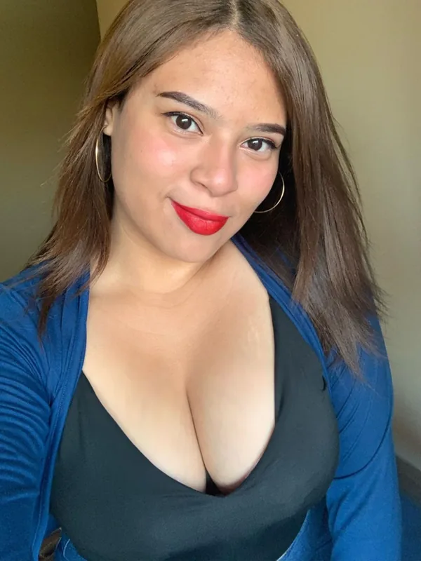Portrait d'une femme aux cheveux bruns portant un haut noir et une veste bleue, regardant l'objectif avec un sourire.