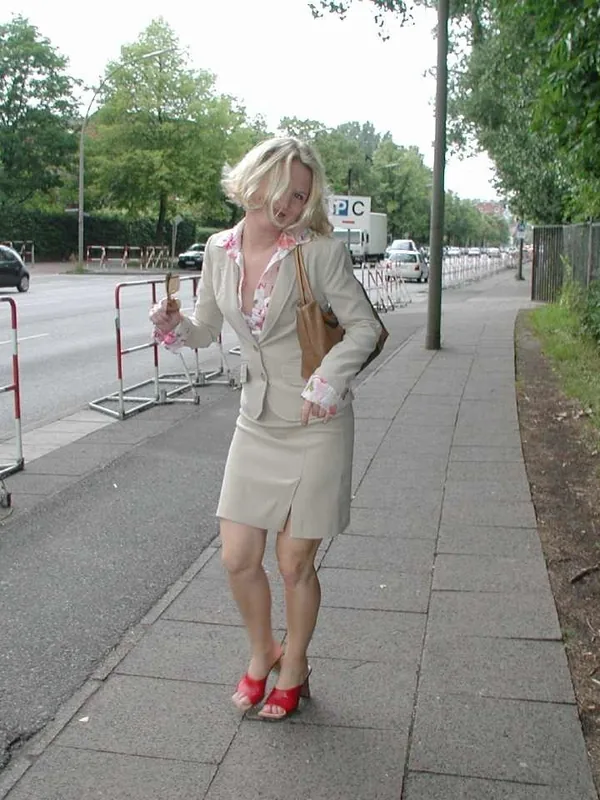 Femme blonde en tenue beige marchant sur un trottoir urbain, regardant l'objectif.