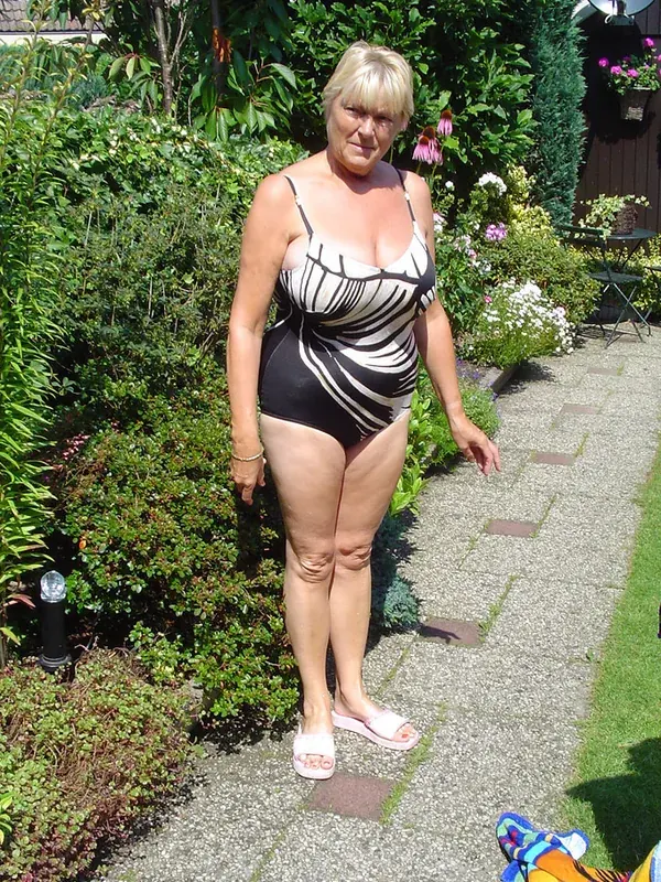 Femme en maillot de bain noir et blanc debout sur un chemin de jardin ensoleillé.