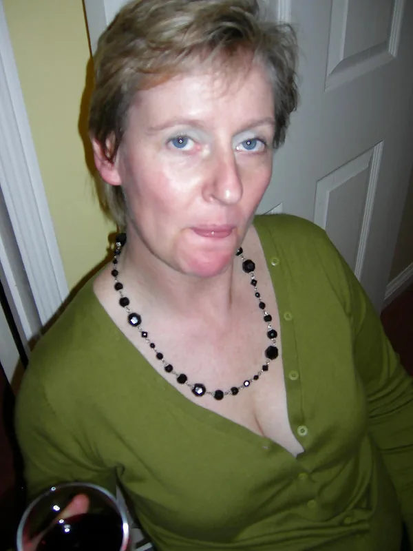 Portrait d'une femme aux cheveux courts blonds, portant un haut vert et un collier noir, regardant l'objectif.