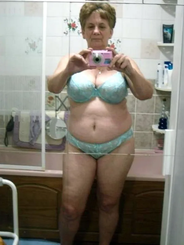 Femme en lingerie bleue prenant un selfie dans un miroir de salle de bain avec un appareil photo rose.