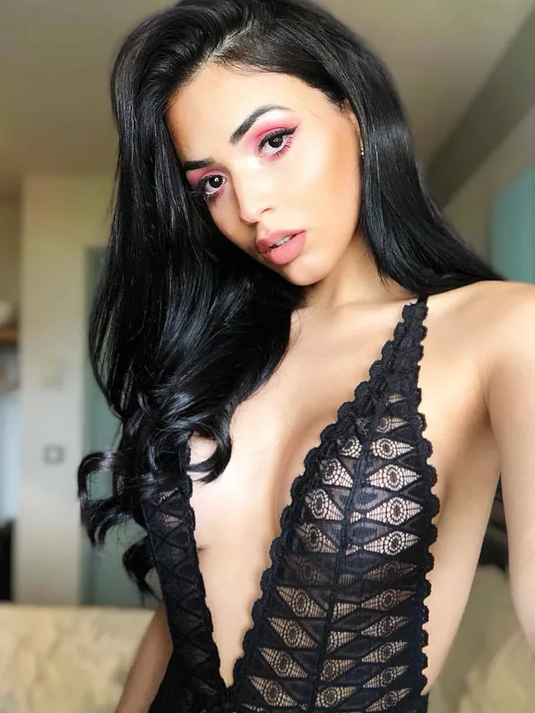 Portrait d'une femme aux cheveux noirs portant une tenue en dentelle noire, regardant l'objectif dans un intérieur éclairé.
