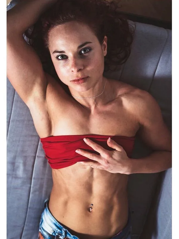 Femme allongée sur un canapé, portant un haut rouge et un short coloré, regardant l'objectif.