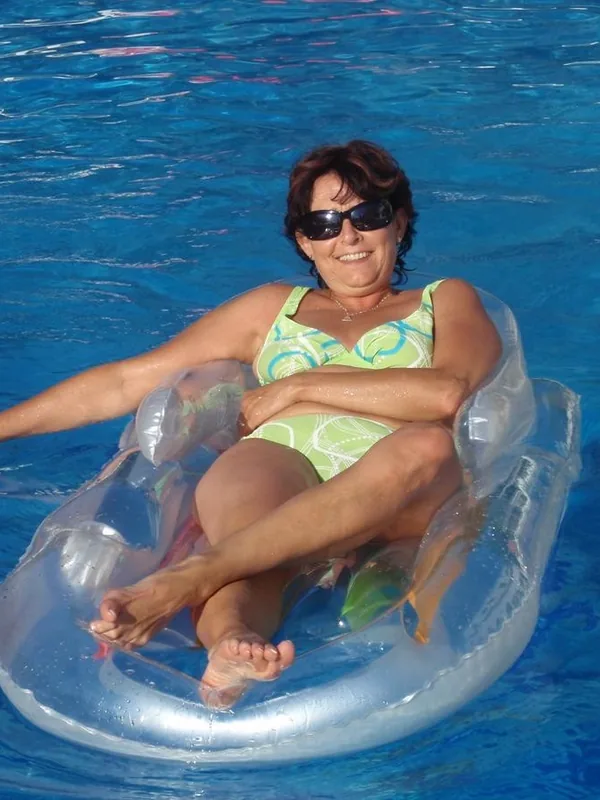 Femme en maillot de bain vert flottant sur un matelas gonflable transparent dans une piscine bleue.