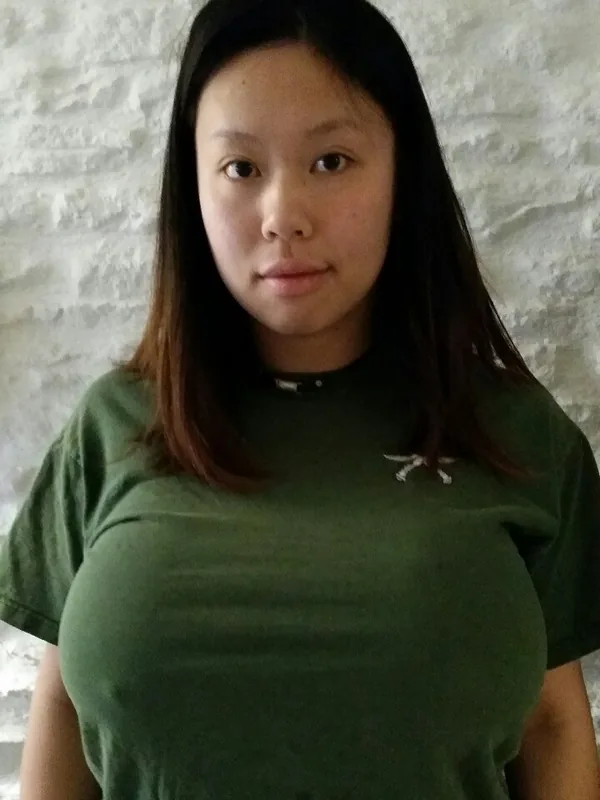 Portrait d'une femme aux cheveux longs portant un t-shirt vert, regardant l'objectif devant un mur texturé.