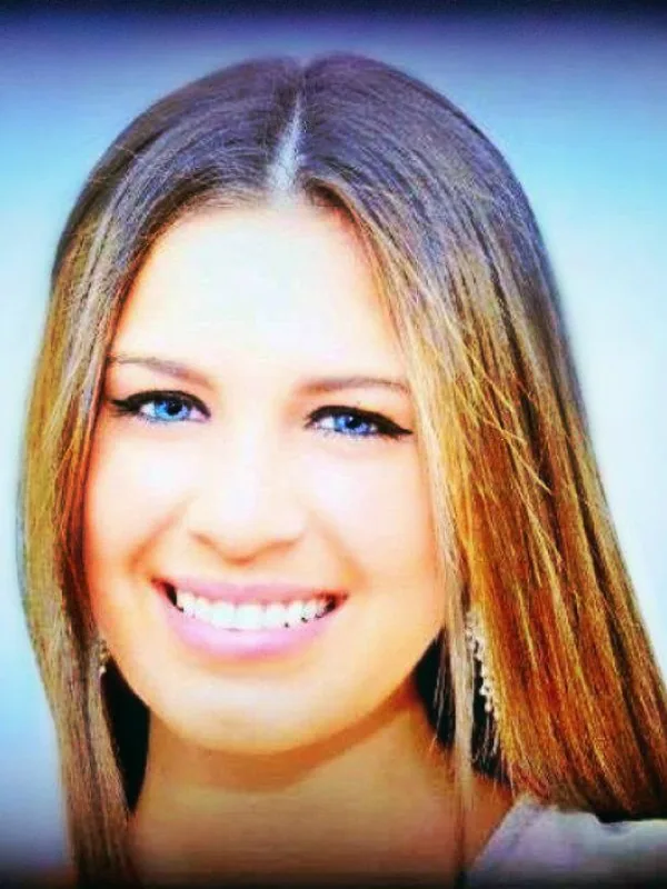 Portrait en gros plan d'une jeune femme souriante aux cheveux bruns et yeux bleus, sur fond bleu clair.
