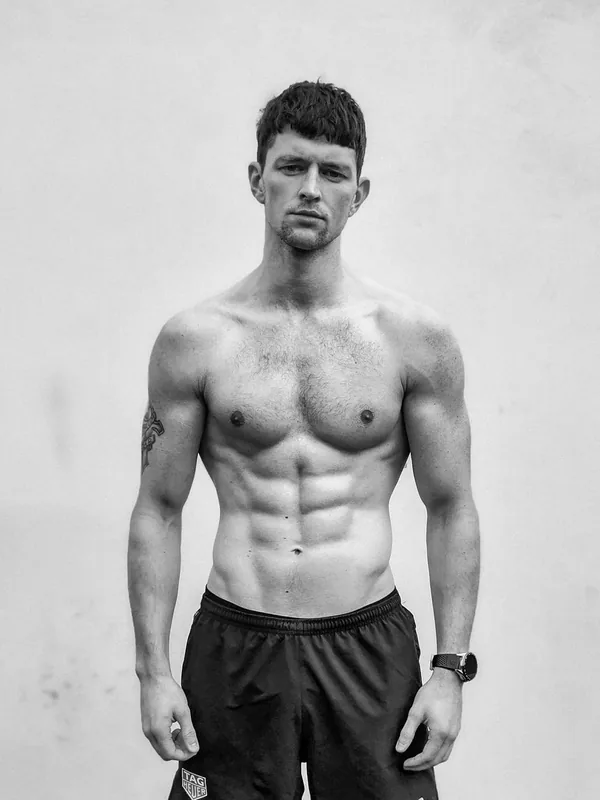 Portrait en noir et blanc d'un homme torse nu, portant un short de sport, regardant l'objectif.