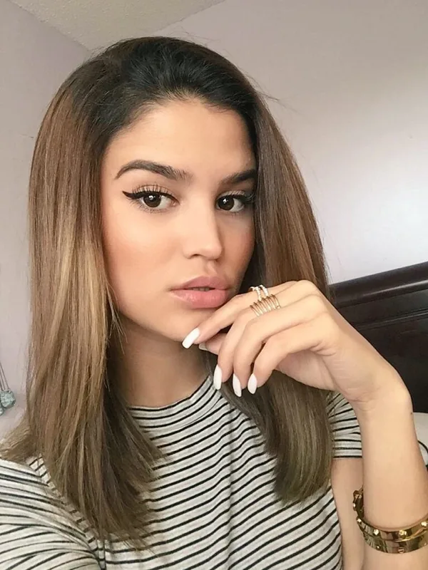 Portrait d'une jeune femme aux cheveux bruns, regardant l'objectif, portant un haut rayé et des bijoux fins.