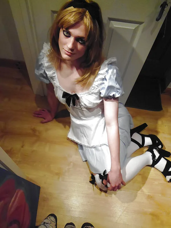 Femme en robe blanche et collants blancs agenouillée sur un sol en bois, regardant vers l'objectif.